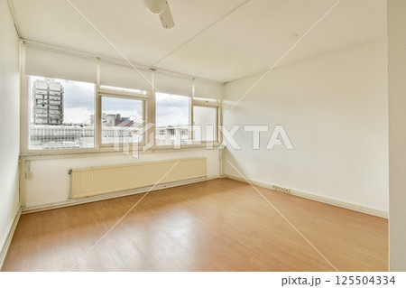 A spacious, well-lit room featuring large windows and minimal decor. The clean lines and soft colors create a tranquil atmosphere perfect for relaxation. 125504334