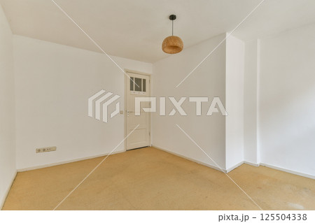 A clean, minimalist interior featuring neutral tones, a simple light fixture, and a door, providing a spacious and uncluttered ambiance. 125504338