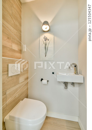 A sleek and contemporary bathroom featuring a wall-mounted sink, elegant lighting, and wooden accents that enhance the minimalist aesthetic. 125504347