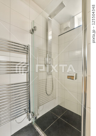 A sleek and modern shower room featuring a glass enclosure, chrome fixtures, and contemporary tiles, creating a minimalist aesthetic. 125504348