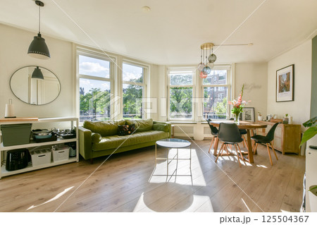 A spacious living room featuring large windows that allow natural light, a comfortable green sofa, and stylish decor elements that enhance the inviting atmosphere. 125504367