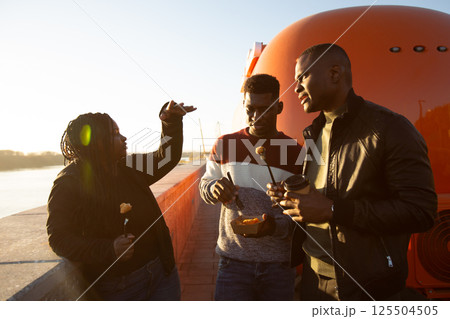 African american friends sharing fried snacks from a takeaway box, using forks. 125504505