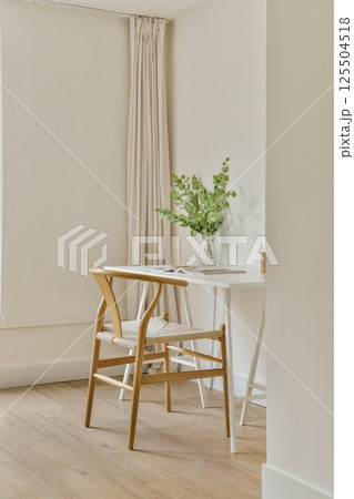 A bright and airy dining area showcasing a wooden chair and table adorned with a simple vase of green plants, highlighting minimalistic design and natural light. A bright and airy dining area showcasing a wooden chair and table adorned with a simple vase of green plants, highlighting minimalistic design and natural light. 125504518
