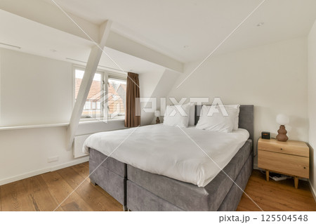 A stylish modern bedroom featuring a cozy bed, large windows for natural light, and minimalistic decor. The use of soft colors creates a serene atmosphere. A stylish modern bedroom featuring a cozy bed, large windows for natural light, and minimalistic decor. The use of soft colors creates a serene atmosphere. 125504548