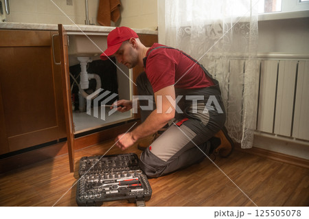 Plumber fixing leaky sink in kitchen Plumber fixing leaky sink in kitchen 125505078