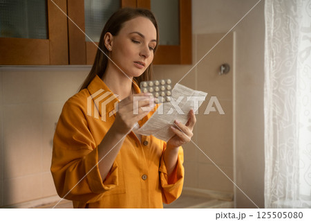 Woman reading medicine instructions in kitchen Woman reading medicine instructions in kitchen 125505080