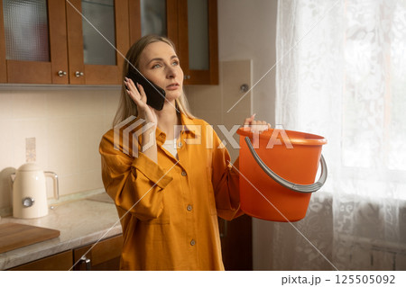Woman calling for help while holding bucket under water leak Woman calling for help while holding bucket under water leak 125505092