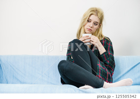 Sad lonely woman sitting on couch with mug 125505342