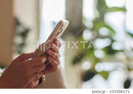 A person is comfortably using their smartphone while sitting in a cozy, relaxed environment A person is comfortably using their smartphone while sitting in a cozy, relaxed environment 125506171