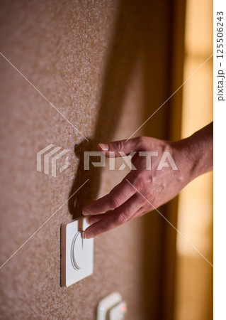 A hand reaches for the light switch in a cozy room, adding warmth and brightness A hand reaches for the light switch in a cozy room, adding warmth and brightness 125506243