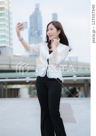 Young woman taking a selfie with a city skyline in the background, showcasing modern urban lifestyle. 125507840