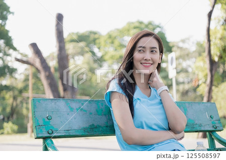 A woman sitting on a park bench, smiling and enjoying the serene surroundings on a sunny day. 125508597