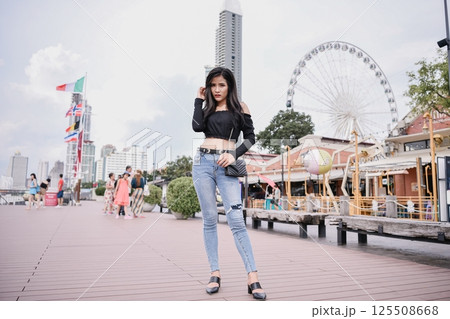 A fashionable woman posing confidently on a waterfront promenade with a ferris wheel in the background. 125508668
