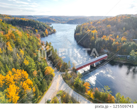 Small red bridge elegantly spanning a serene river in a vibrant autumn forest with colorful foliage 125509743