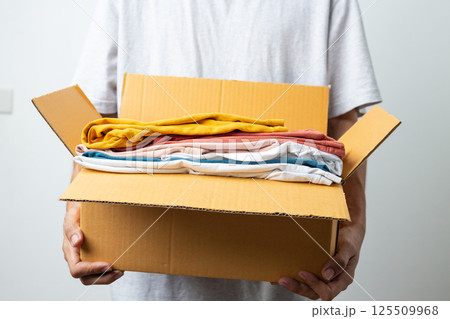 Donation Concept, man holding clothes with donate box in white background room. 125509968