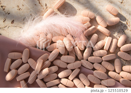 Pills or vitamins on the natural wood background with pink silk fabric and feather in summer day. Top view.  125510529