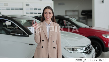 Professional car saleswoman holding car keys standing near new cars at the dealership. Concept of car shopping, buying, and dealership. Professional car saleswoman holding car keys standing near new cars at the dealership. Concept of car shopping, buying, and dealership. 125510768