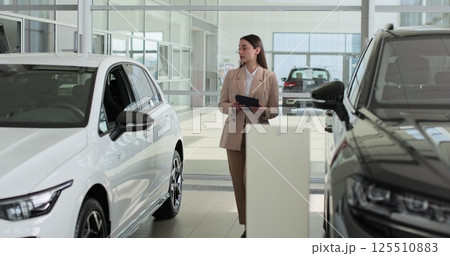 Woman holding clipboard document saleswoman analyzing dealer showroom auto automobile new car rental service. 125510883