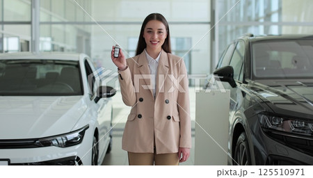Professional car saleswoman holding car keys standing near new cars at the dealership. Concept of car shopping, buying, and dealership. 125510971