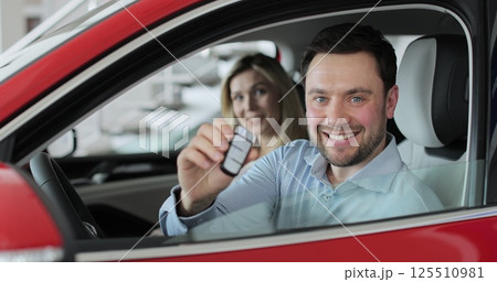 Young man showing key to new car. Happy couple family buyers clients. Auto business concept. Man holding car keys at the dealership salon. 125510981