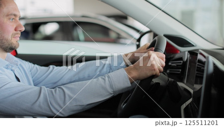 Young man auto driver car owner holding steering wheel buy new automobile dealership inside vehicle. Concept of car shopping, buying, and dealership. 125511201