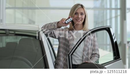Happy woman standing at dealership near new car. Handsome young female choosing transport to buy. Concept of car shopping, buying, and dealership. 125511218