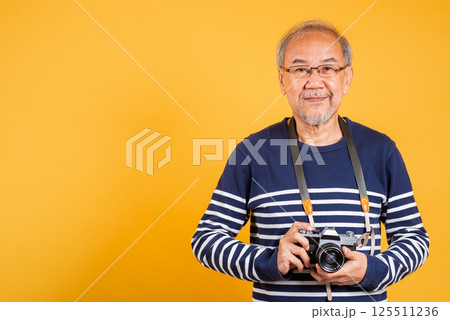 Portrait Asian old man wearing glasses holding vintage SLR camera studio shot isolated yellow background, smiling happy Photographer elderly man gray haired holds old fashioned camera Portrait Asian old man wearing glasses holding vintage SLR camera studio shot isolated yellow background, smiling happy Photographer elderly man gray haired holds old fashioned camera 125511236