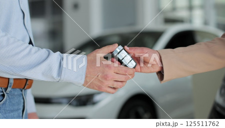 Close up woman hand gives a car keys to man hand in car dealership close up. Concept of car shopping, buying, and dealership. 125511762