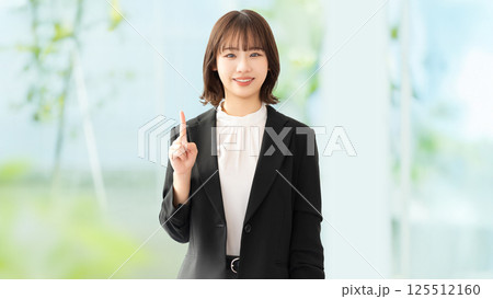 人差し指を立てて案内する笑顔の女性・ビジネスウーマン 人差し指を立てて案内する笑顔の女性・ビジネスウーマン 125512160