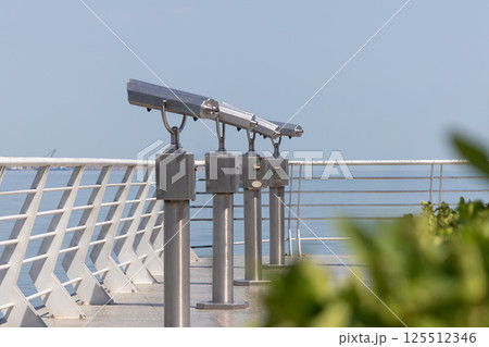 Coin operated binoculars overlooking tranquil sea on sunny day Coin operated binoculars overlooking tranquil sea on sunny day 125512346