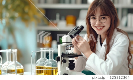 A smiling female scientist uses a microscope in a bright lab. 125512364