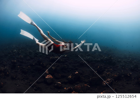 Woman freedives in sea. Slim female freediver swims underwater in deep ocean 125512654