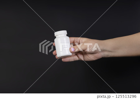white jar with medicines in hand on dark background 125513296
