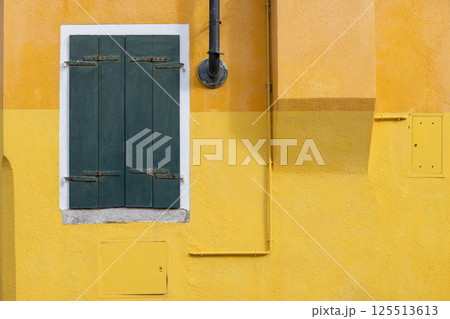 Yellow textured wall with green closed shutters in Burano Italy 125513613