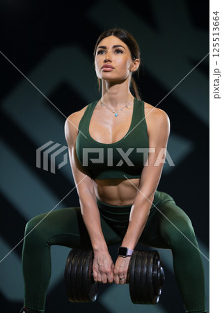 fitness enthusiast demonstrates strength and determination while lifting heavy dumbbell in gym setting. individual wears matching athletic gear and showcases toned muscles. 125513664