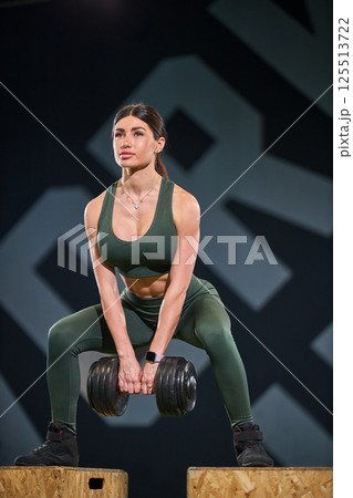 fit person is engaging in deadlift exercise using dumbbell in well equipped fitness center. individual displays focus and strength while maintaining proper form. 125513722