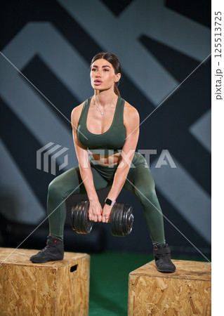 woman engages in squat exercise while holding dumbbells in fitness setting. She is focused and determined as she works on her strength training routine. woman engages in squat exercise while holding dumbbells in fitness setting. She is focused and determined as she works on her strength training routine. 125513725