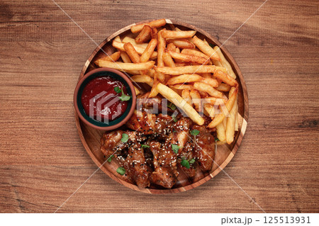 barbecue chicken wings, sprinkled with sesame seeds, with French fries, and sauce, on a wooden plate, rustic style, barbecue chicken wings, sprinkled with sesame seeds, with French fries, and sauce, on a wooden plate, rustic style, 125513931