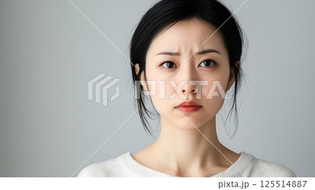 Close up portrait of an Asian girl with black hair and wearing a white sweater, a concerned worried look on her face 125514887