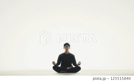 Distant shot of an Asian man in a black suit sitting in lotus pose on a white background Distant shot of an Asian man in a black suit sitting in lotus pose on a white background 125515840