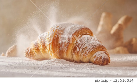 A golden croissant rests on a wooden table, dusted with flour. The warm kitchen atmosphere emphasizes the freshness of the pastry, inviting indulgence and comfort 125516014