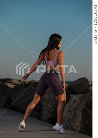 person enjoying their wellness journey stretches near rocky shore. warm colors of sunset create serene atmosphere for fitness and mindfulness ocean. 125516843
