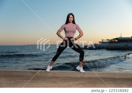 woman in athletic attire stands confidently on sandy shore posing hands on hips. woman in athletic attire stands confidently on sandy shore posing hands on hips. 125516892