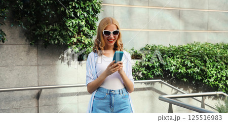 Stylish modern happy smiling young woman with phone in city park, girl holding smartphone on street 125516983
