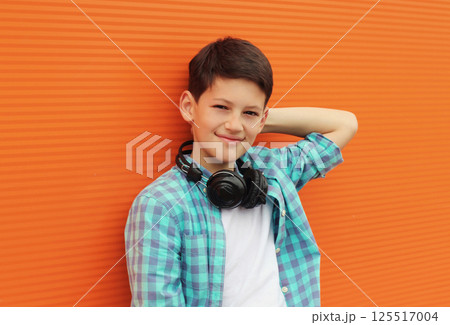 Portrait of happy modern teenage boy listening to music with headphones on orange wall background Portrait of happy modern teenage boy listening to music with headphones on orange wall background 125517004