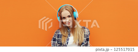 Summer portrait happy modern young woman listening to music with headphones on orange background Summer portrait happy modern young woman listening to music with headphones on orange background 125517015
