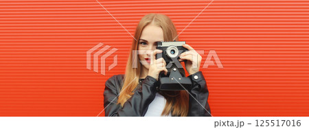 Portrait of stylish young woman photographer with film camera, modern girl taking a picture on red 125517016
