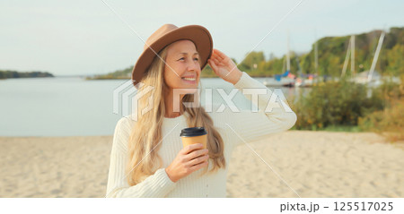 Stylish happy woman with cup of coffee drink on beach, smiles, looking away on sea coast background Stylish happy woman with cup of coffee drink on beach, smiles, looking away on sea coast background 125517025