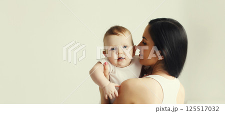 Happy young mother holding cute baby together in white room at home Happy young mother holding cute baby together in white room at home 125517032