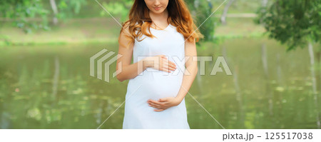 Close-up happy young pregnant woman walking in summer park 125517038
